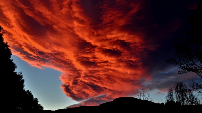 Fiery sunset clouds over silhouetted hills and trees