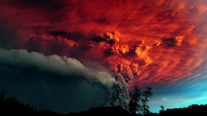 Volcanic eruption with red clouds and silhouetted trees