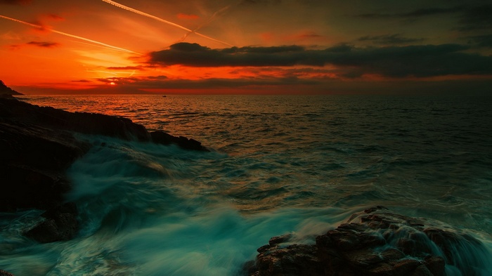 Sunset over the ocean with waves crashing on rocks
