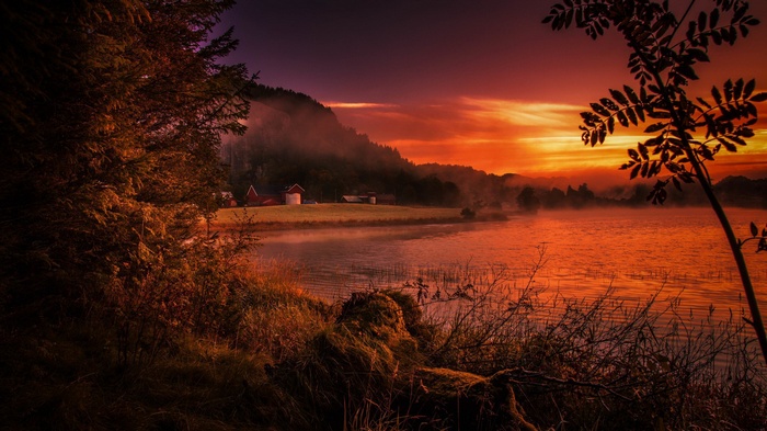 Sunset over a misty lake with farm buildings