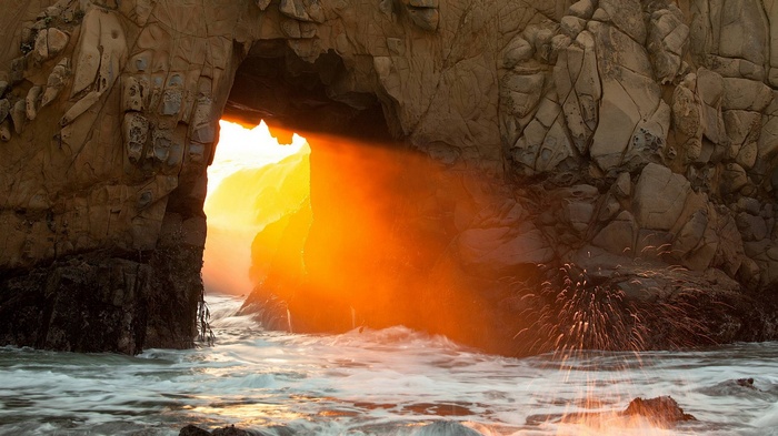Sunlight beams through a sea cave archway
