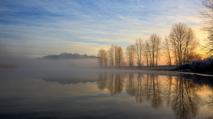 Misty lake with trees and mountains at sunrise