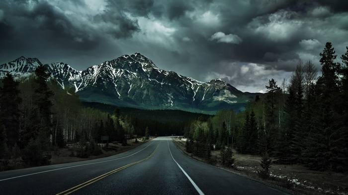 Road leading to snow-capped mountains under stormy clouds