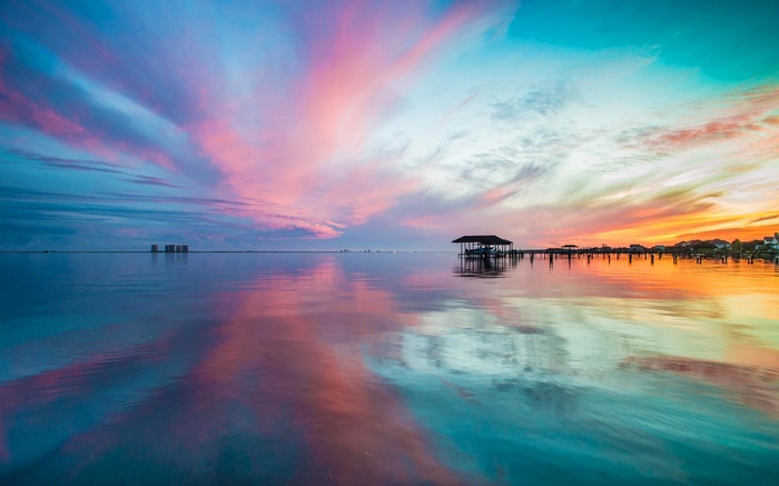Sunset over a calm bay with a pier and boathouse