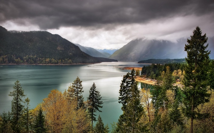 Lake surrounded by mountains and evergreen trees under cloudy sky