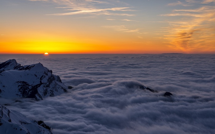 Sunset over clouds with snow-capped mountains