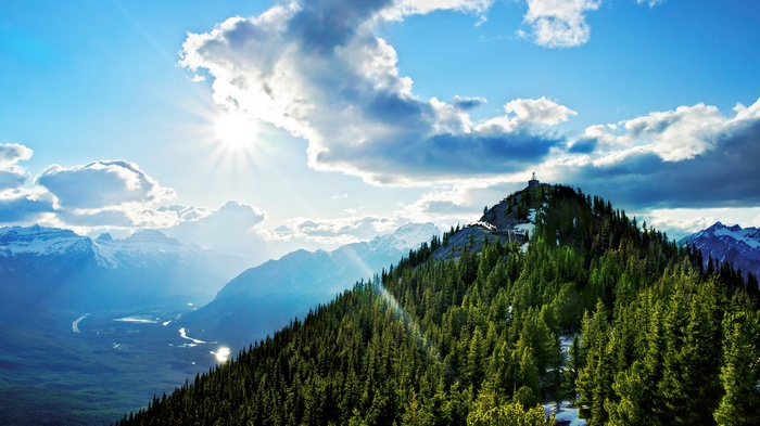 Mountain peak with trees and sunlit clouds