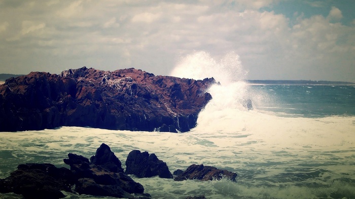 Waves crashing against rocky shore under cloudy sky