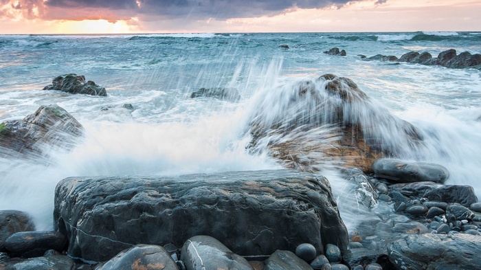 Waves crashing on rocky shore at sunset
