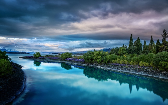 Lake with mountains and trees under cloudy sky