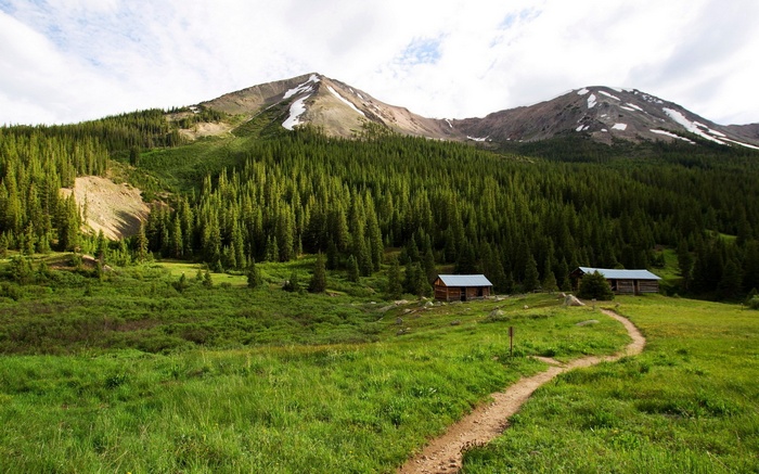 Two wooden cabins in a mountain valley with a dirt path