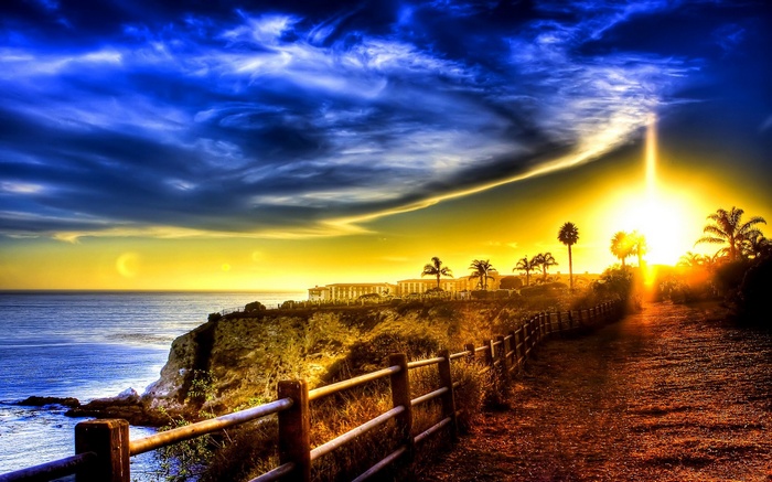 Sunset over the ocean with a coastal path and buildings