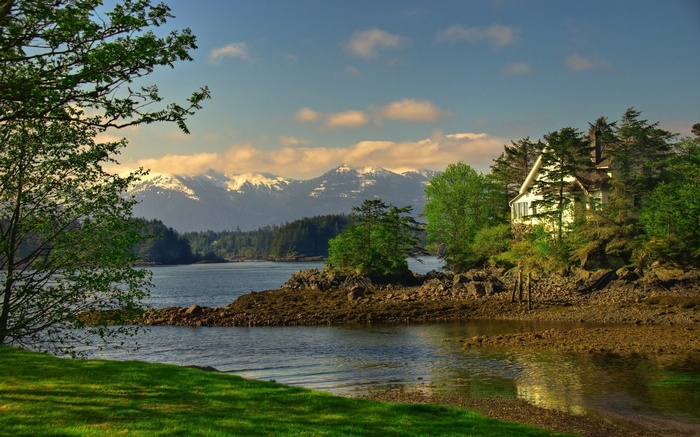 House on a rocky shore with snow-capped mountains