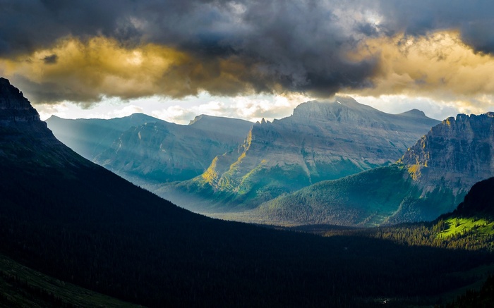 Sunlight beams through clouds onto mountains and forest