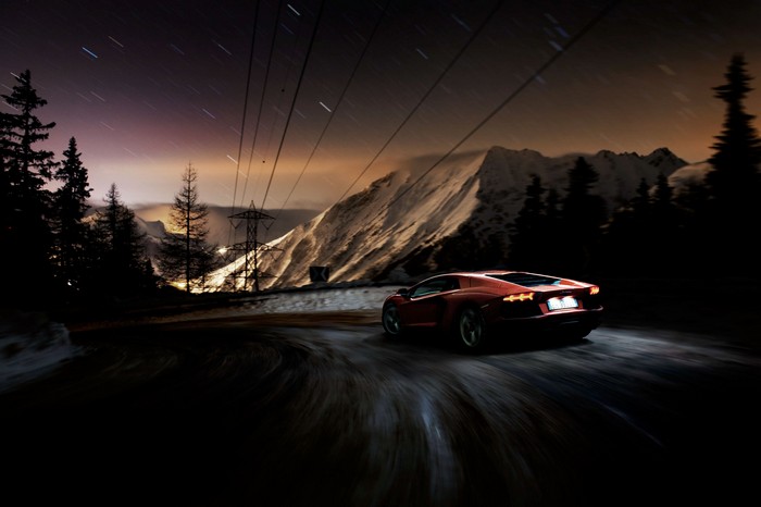Red Lamborghini Aventador driving on a mountain road at night