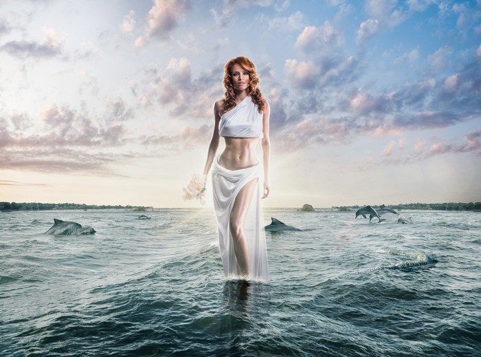 Woman in white dress walking in the ocean with dolphins