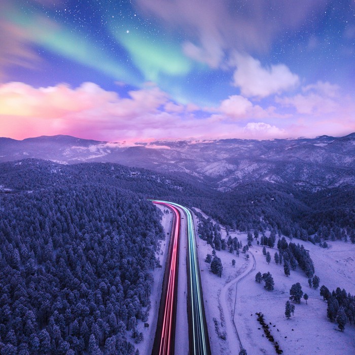 Long exposure road with aurora borealis over snowy mountains