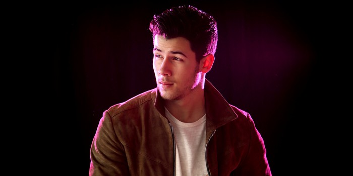 Nick Jonas in brown jacket with pink lighting