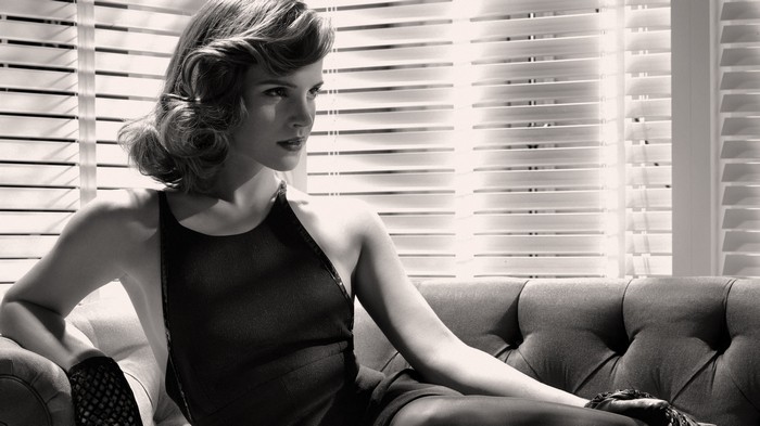Emma Watson in a black dress sitting on a couch
