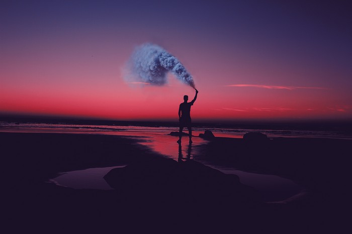 Person holding smoke bomb on beach at sunset
