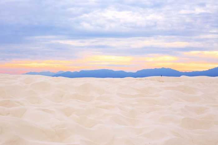 Sand dunes at sunset with mountains and clouds