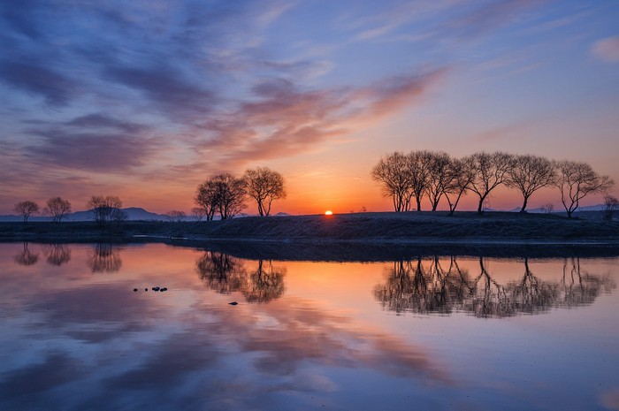 Sunrise over a calm lake with trees and reflections