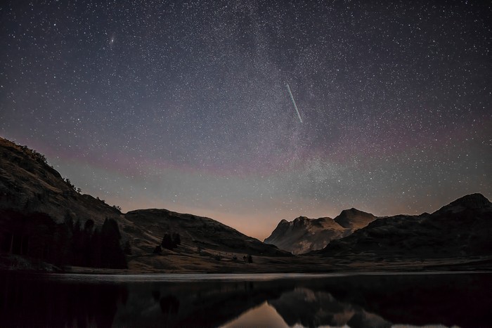 Mountains and shooting star over lake at night