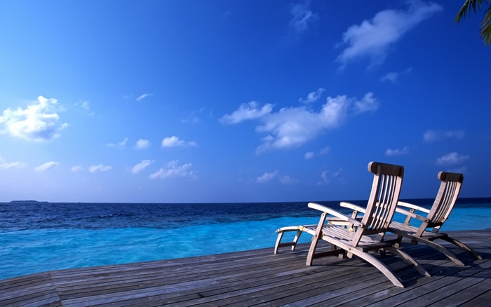 Two lounge chairs on a wooden deck overlooking the ocean