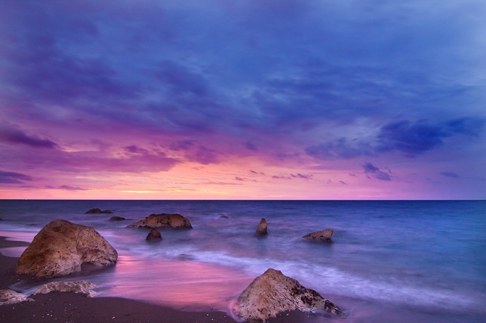 Sunset over the ocean with rocks on the seashore