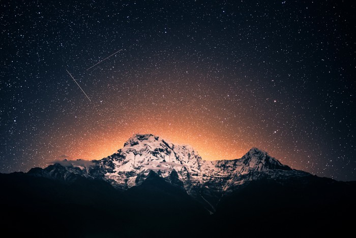 Snow-capped mountains under a starry sky with shooting stars