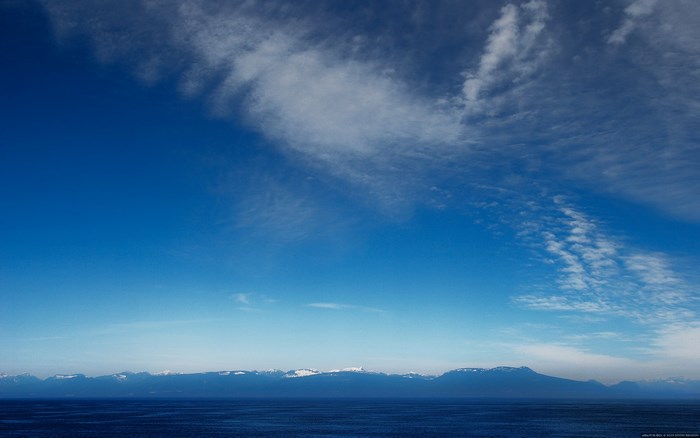 Vast blue sky over ocean and snow-capped mountains