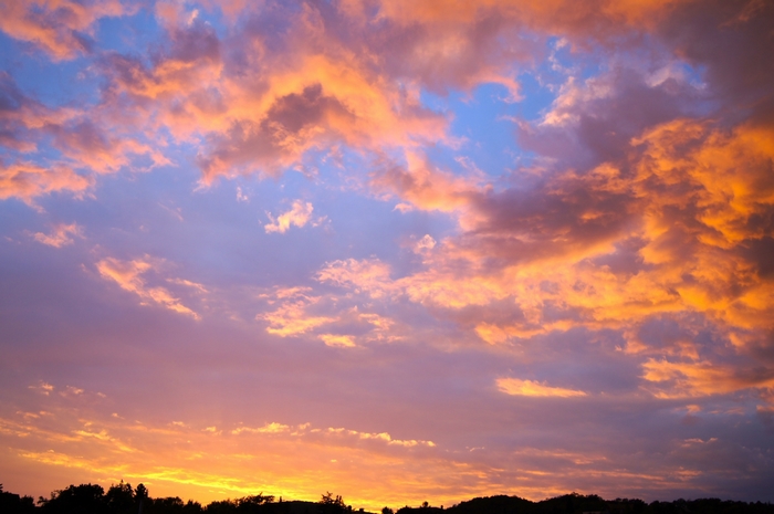 Sunset clouds over silhouetted trees and hills