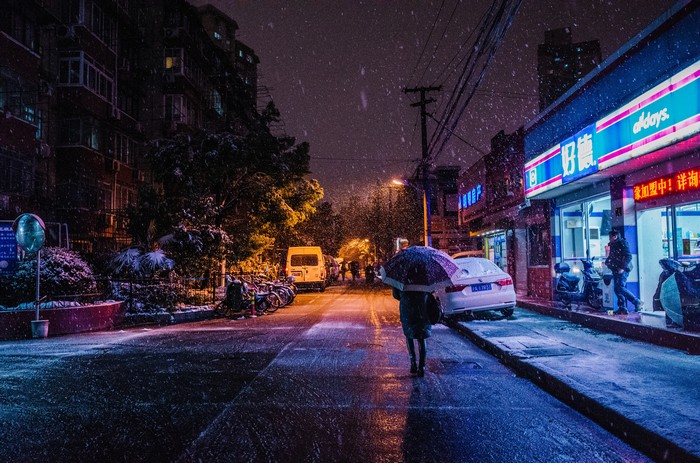 Snowy night street with people and a convenience store