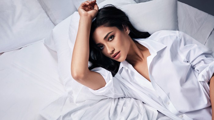 Shay Mitchell lying on a bed in a white shirt