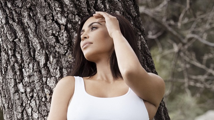 Kim Kardashian leans against a tree