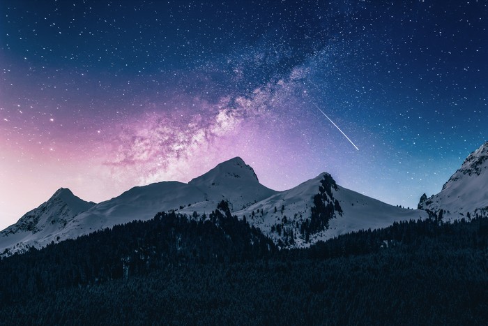 Milky Way over snow-capped mountains and forest