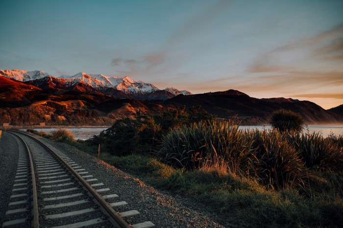 Railroad Tracks Leading to Snowy Mountains at Sunset 4K