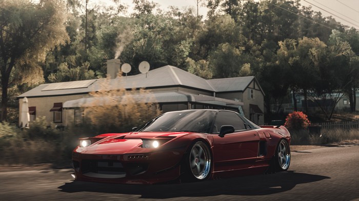 Red Acura NSX driving on a road with a house in the background