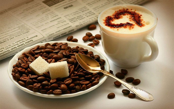 Coffee beans, sugar cubes, spoon, and cappuccino with heart art