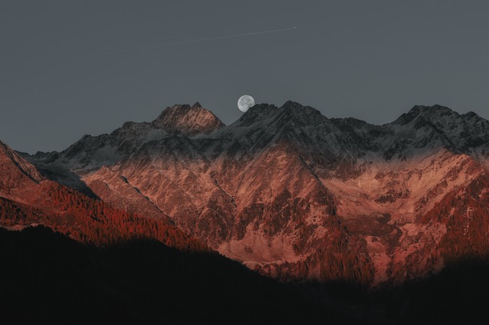Moon over snow-capped mountains at sunset