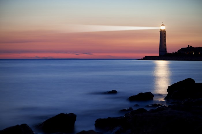 Lighthouse shining light over the ocean at sunset