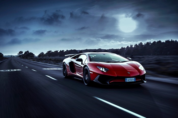 Red Lamborghini Aventador driving on a road at night