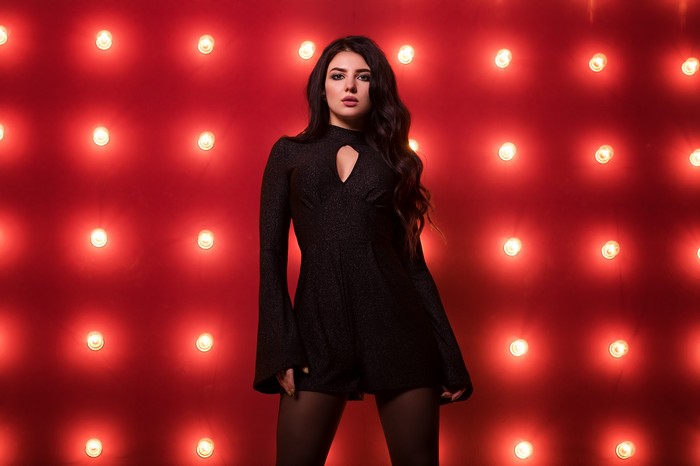 Woman in a black dress posing against a red backdrop