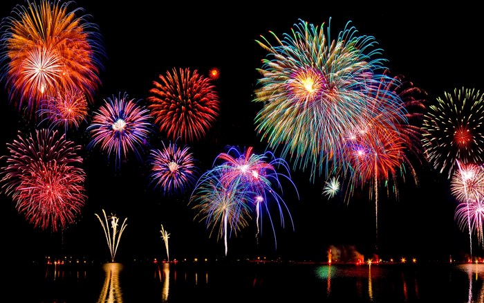 Colorful fireworks explode over a dark body of water