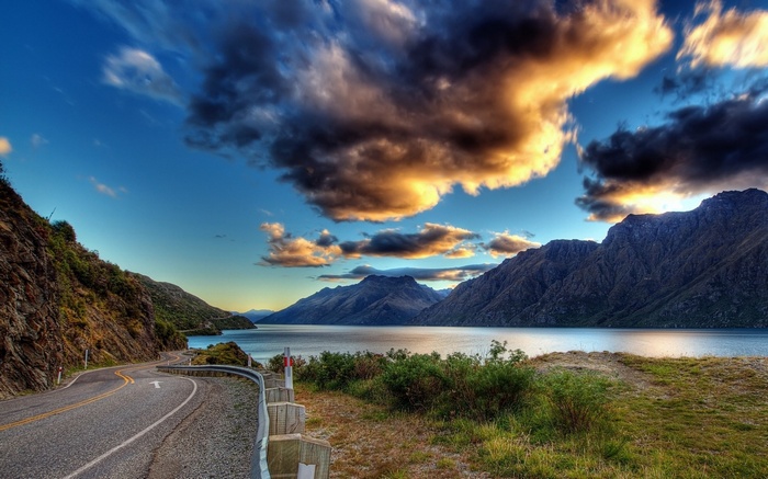 Winding road along a lake with mountains and dramatic clouds