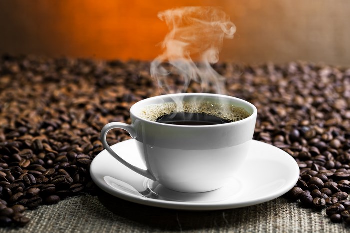 Steaming cup of coffee on a bed of coffee beans