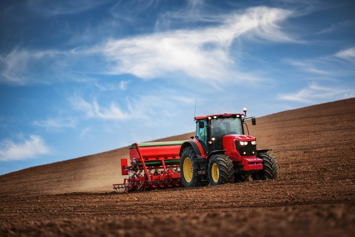 Red tractor plowing a field under a blue sky