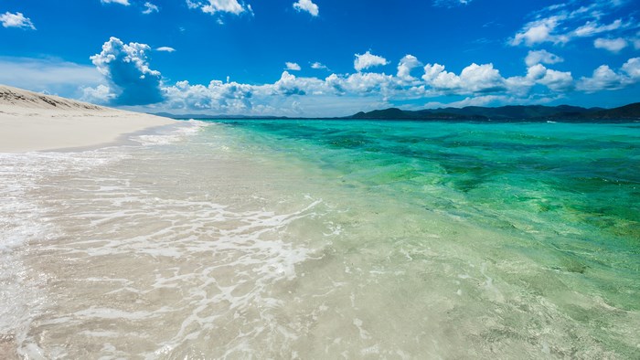 Turquoise ocean waves lap on a white sand beach under a blue sky.