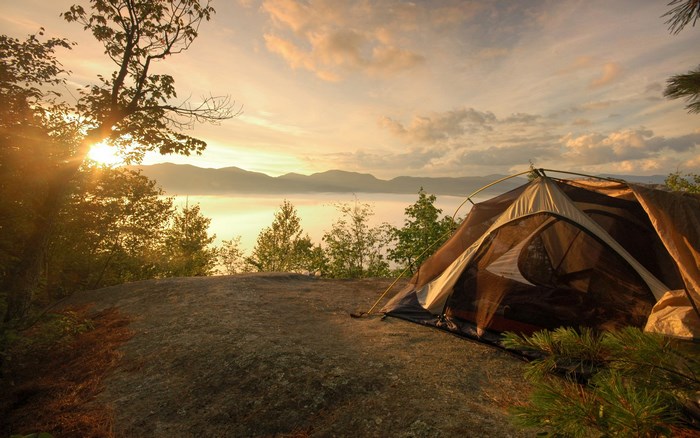 Tent camping at sunrise overlooking a misty lake and mountains