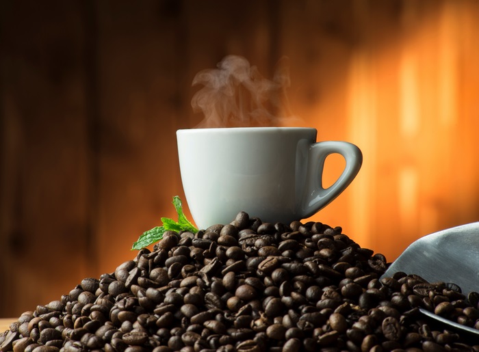 Steaming cup of coffee on roasted coffee beans